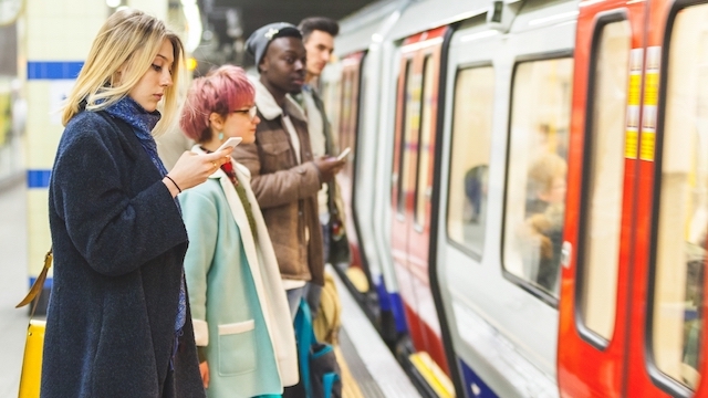 Woman looking at her mobile phone next to a Tube train on a busy platform at a London Underground station