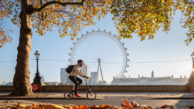 A man cycles past the London Eye on a clear autumn day.