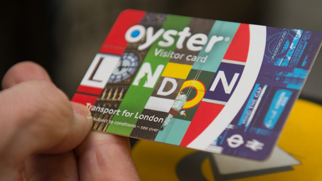 Close-up of a London transport Visitor Oyster Card with a yellow Oyster Card reader in the background.