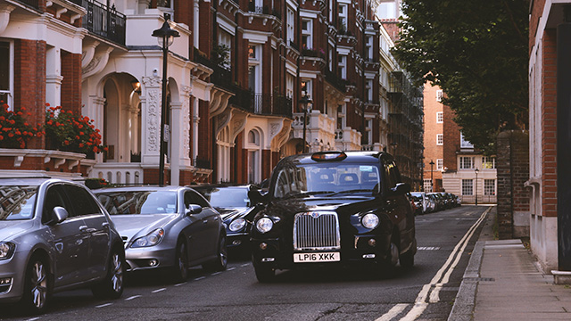 Un taxi noir roule dans une rue de Londres avec d'autres voitures garées sur le côté.