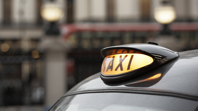 Illuminated yellow taxi sign above the windscreen of a black cab in London.
