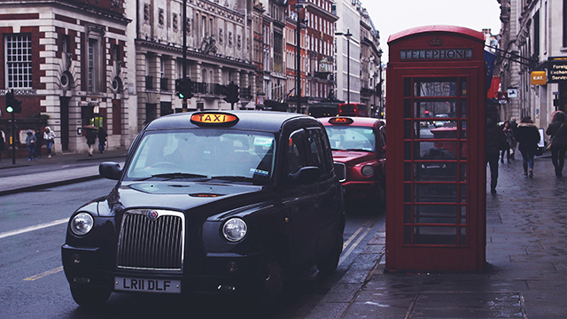 Un taxi traditionnel londonien de couleur noire, le black cab, se tient sur le côté de la route à côté d'une cabine téléphonique rouge.