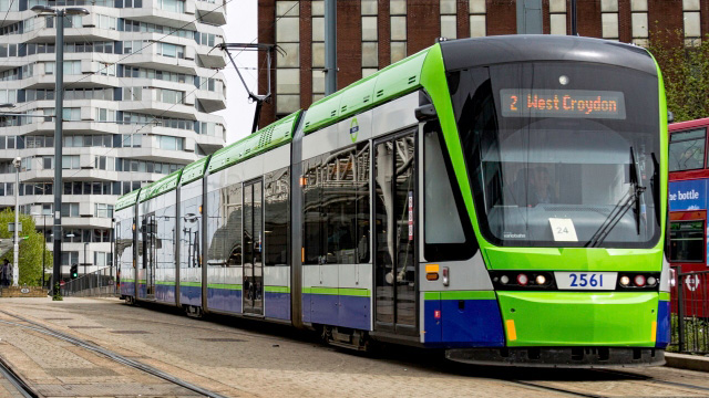 A green, white and blue London tram drives through the city with a sign that reads "West Croydon"