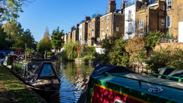 Brightly painted houseboats along Regent's Canal with a line of brown brick houses on the opposite bank. 