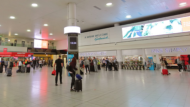 People with luggage gather in a large open space at Gatwick Airport.