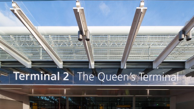 Entrance to Terminal 2 at London Heathrow Airport with large blue and white sign reading 'Terminal 2 The Queen's Terminal'