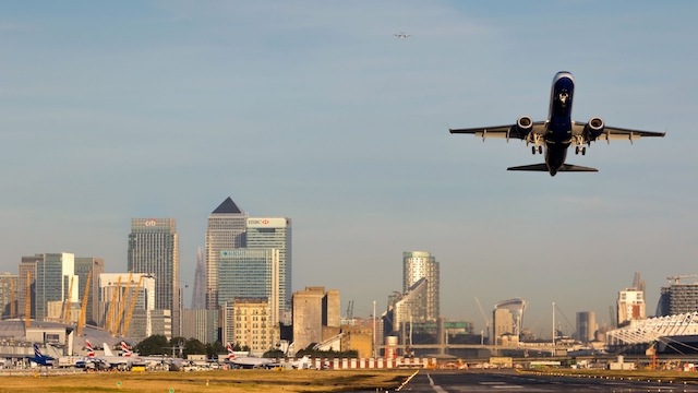 A plane takes off from London City Airport with the skyscrapers of Canary Wharf in the background.