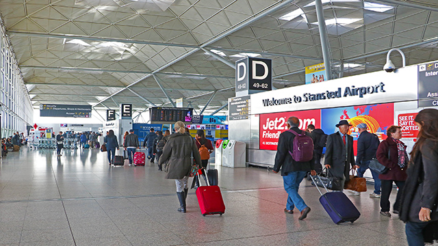 A group of passengers are walking with their suitcases in hands in Stansted arrival hall.