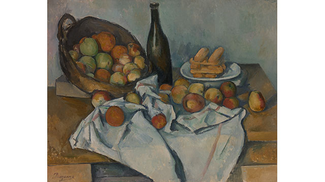 A still life painting of a basket of green, red, orange and yellow apples on a table covered in a table cloth and more apples with a bottle of wine and a plate of food behind