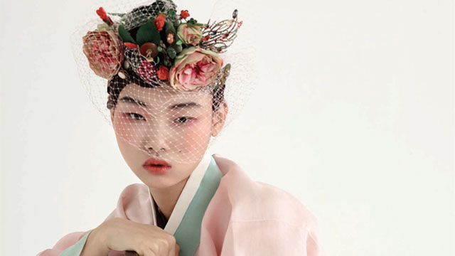 A Korean girl with pink flowers in her hair wearing a pink and green robe.