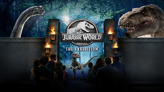 Eine Gruppe von Personen wartet darauf durch die Tore der Ausstellung zu gehen und Dinosaurier stehen an der Seite hinter dem Tor.