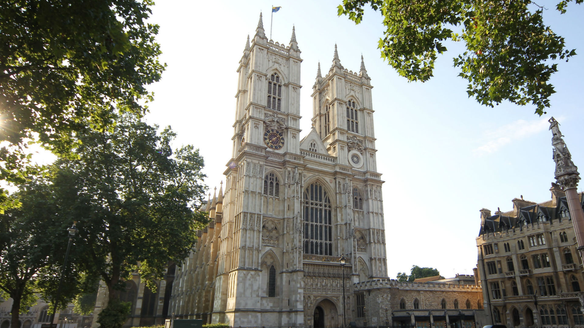 Exterior view of Westminster Abbey with leafy trees and sunshine