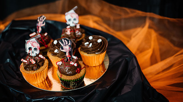 A plate of graveyard cupcakes with skulls and hands on a black and orange table