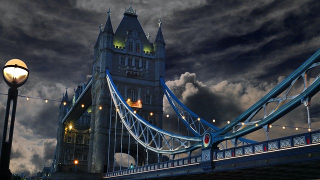 Tower Bridge in a dark setting with dark clouds and the bright blue railings.