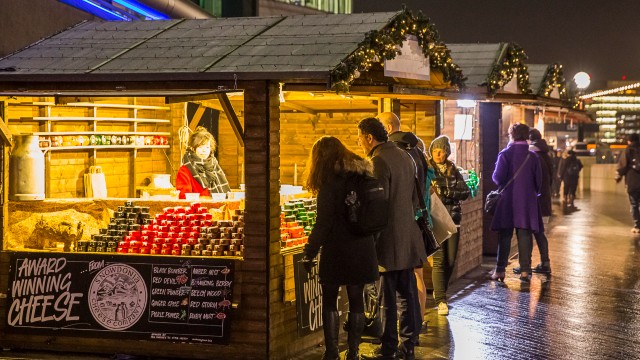 Menschen stehen und stöbern an Weihnachtsmarktständen, die "preisgekrönten Käse" verkaufen 