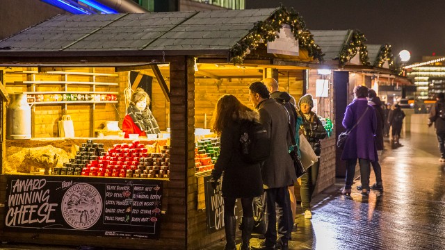 Menschen stehen und stöbern an Weihnachtsmarktständen, die "preisgekrönten Käse" verkaufen