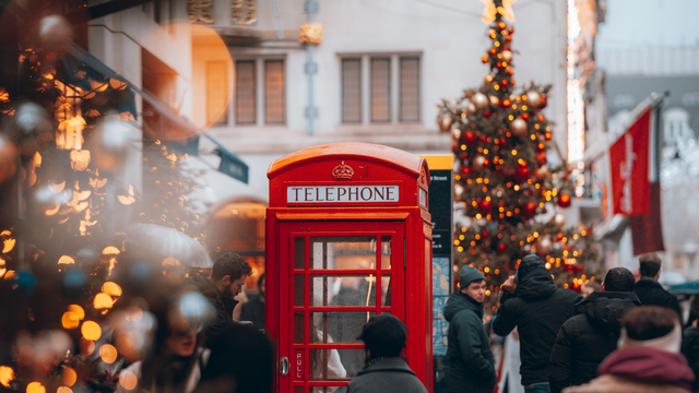 Eine Gruppe läuft durch London, vorbei an einer leuchtend roten Telefonzelle und Weihnachtsbäumen.