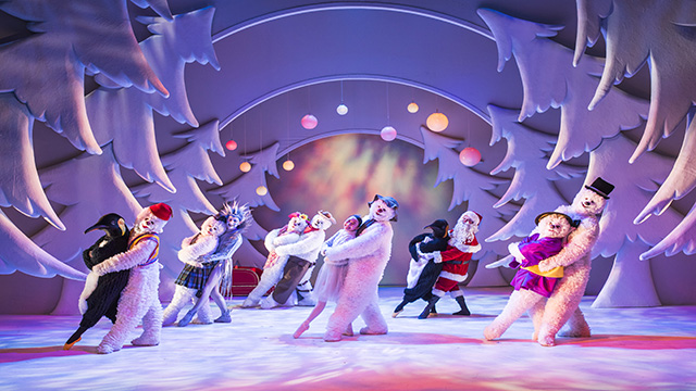 Various Snowmen wearing hats and scarves of different colours are dancing on a stage looking like a snow covered forest.