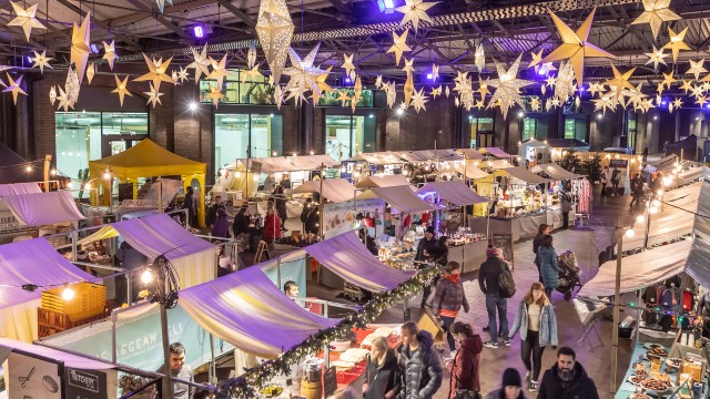 Verschiedene Sternenornamente hängen von der Decke über überdachten Marktständen und warm gekleideten Besuchern.