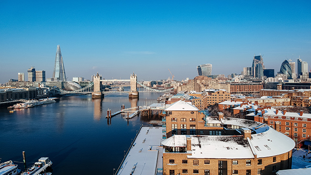Winter skyline of London with the Shard and Tower Bridge in the background and snow on some roofs.