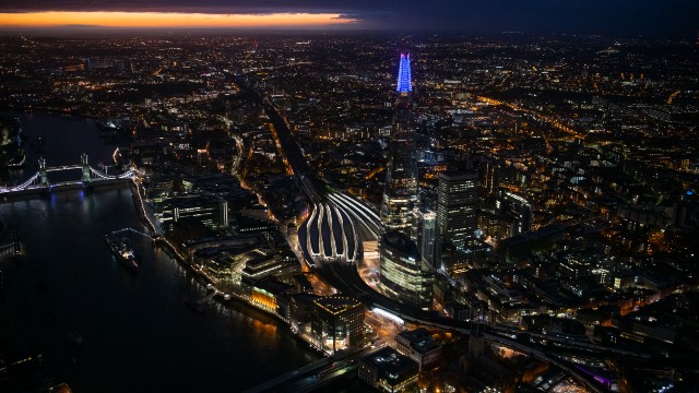 London lit up beside the Thames with the top of the Shard crowned in blue lights.