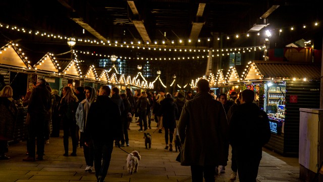 Southbank Centre's Winter Festival. Menschen, die an einem Winterabend um beleuchtete Marktstände spazieren.