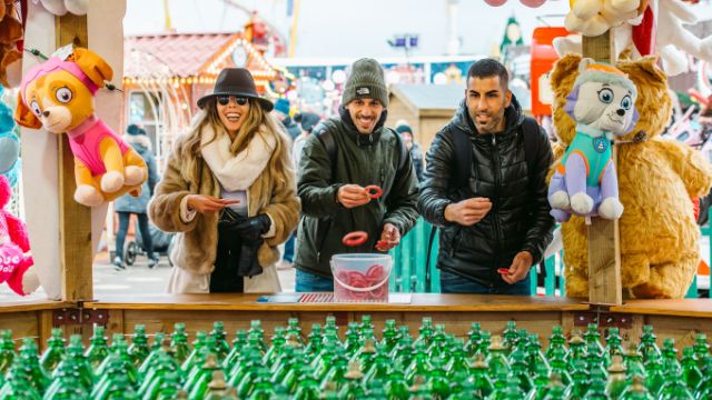Trois personnes tentent de gagner un jeu de lancer d'anneaux à Winter Wonderland à Londres.