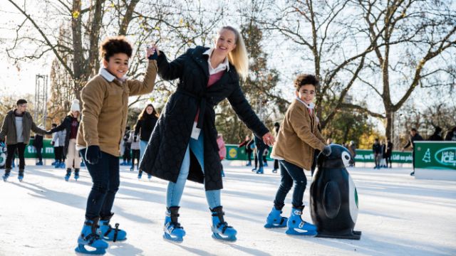 Eine Frau und zwei Kinder fahren Schlittschuh auf der Eislaufbahn im Winter Wonderland in London.