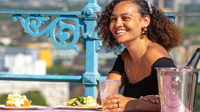 A woman smiling while sitting at a dining table outside.