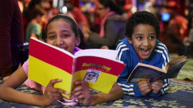 Two children smiling as they read books during the Imagine Children's Festival in Southbank.