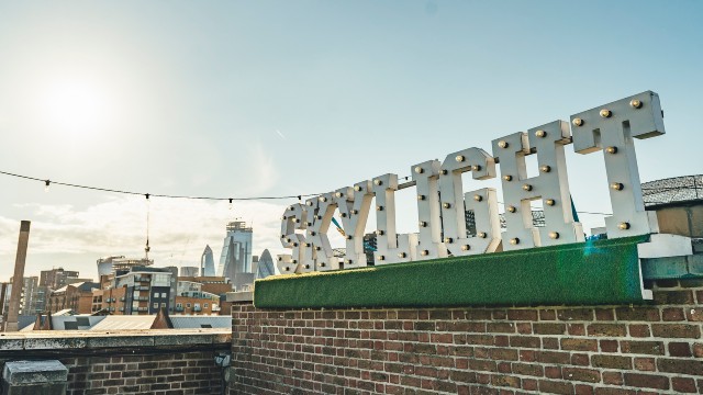 A big sign of the Skylight Rooftop Bar on a sunny day with London panorama in the background.