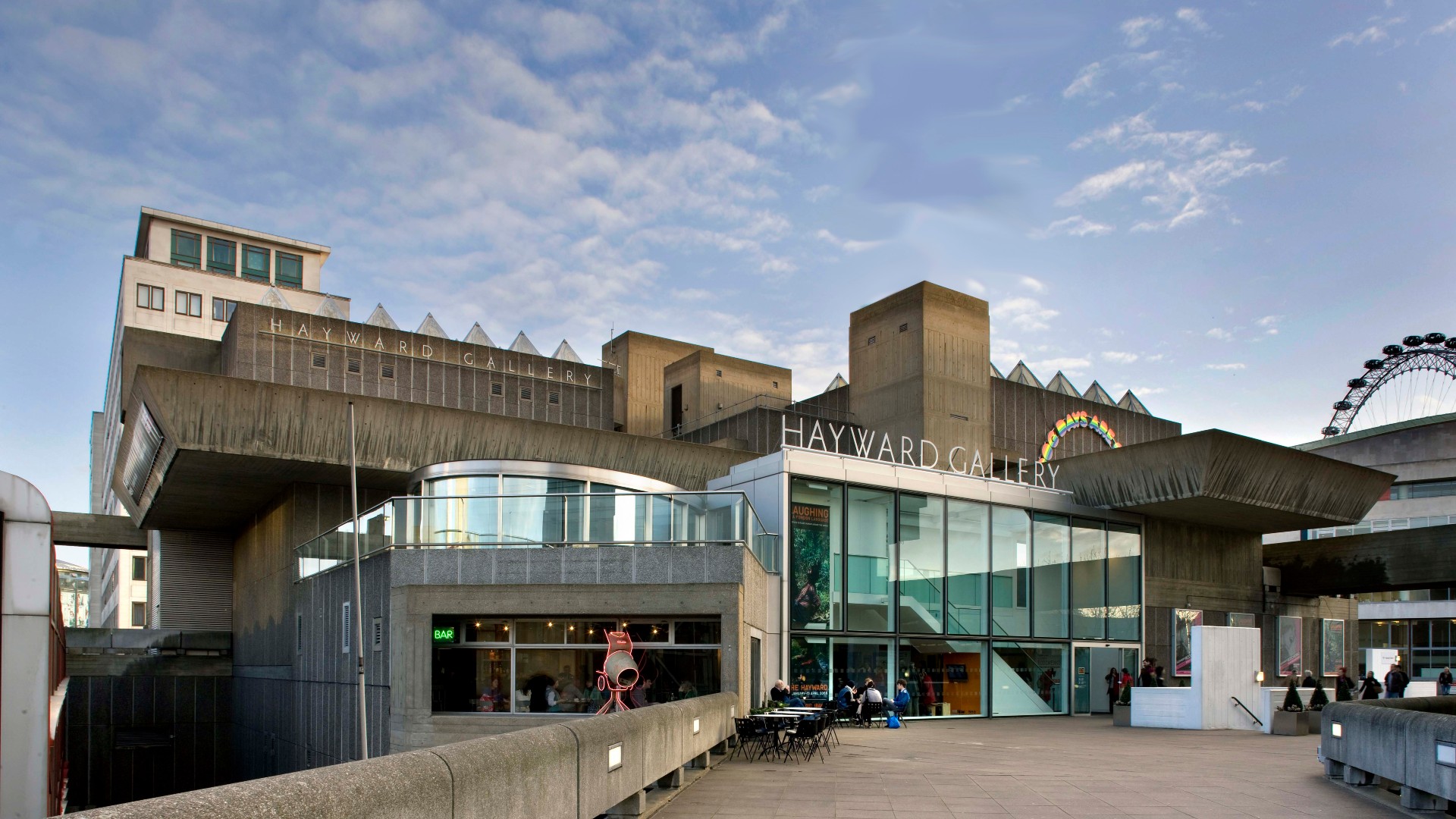 The Southbank Centre's Hayward Gallery on a bright day, with some people sitting at the desks in front of the building.