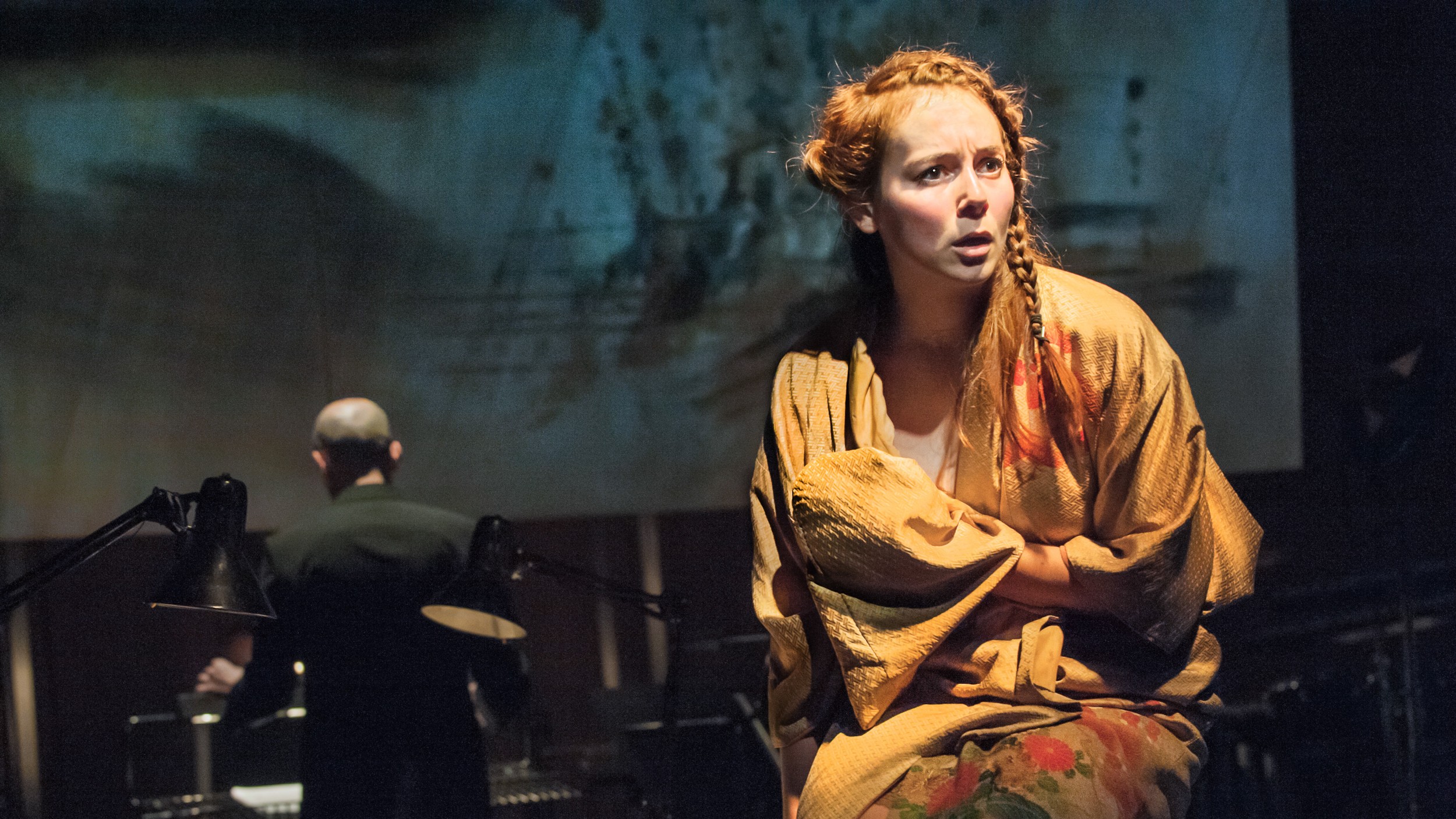 Stream the New Dark Age from home this weekend. Credits: Stephen Cummiskey/Royal Opera House. An actress wearing brown clothes, lit up, with dark background and a man playing the piano.