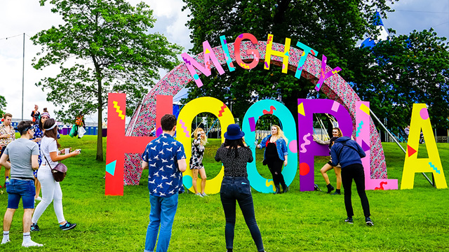 People in front of a colourful sign that says "Mighty Hoopla" at the Mighty Hoopla Music Festival in Brockwell Park, London