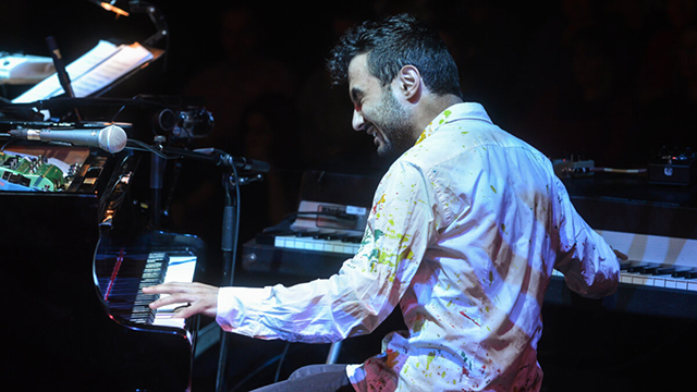 Tigran Hamasyan sitting down and playing two pianos, one with each hand.