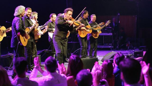 The Gipsy Kings' band members play their violins and guitars on stage in front of a crowd.
