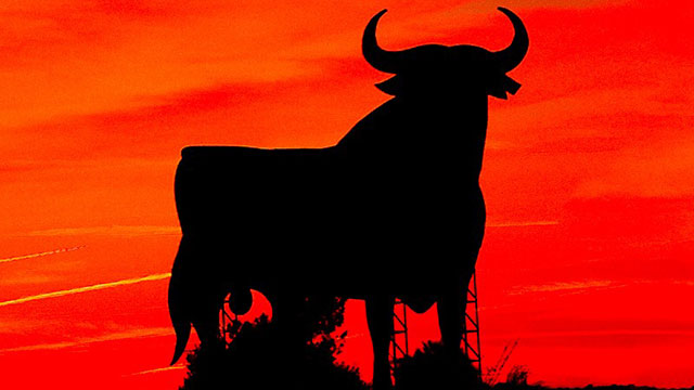A black silhouette of a bull in front of a red background.