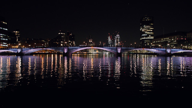 Lambeth Bridge at night lit up with purple lights with the skyline of London in the background