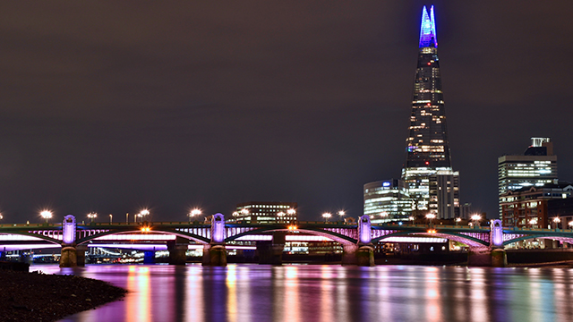 The Shard is illuminated at night with the top of the building lit in a bright blue colour.