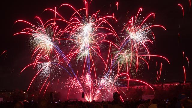 Red fireworks explore above a crowd of people at night.