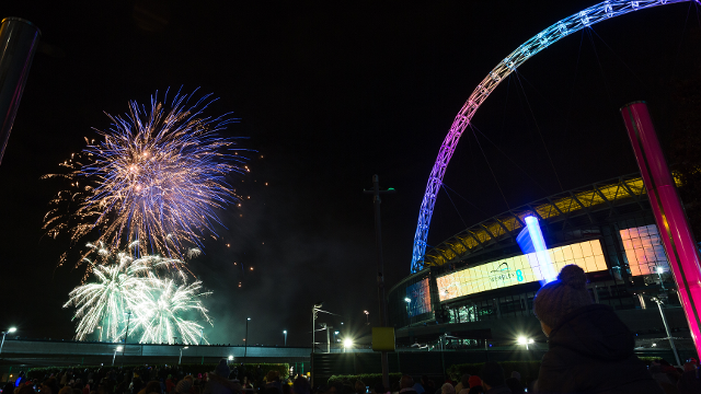 Fireowkrs explore in the distance at night, with Wembley Stadium's illuminated arch in the foreground.