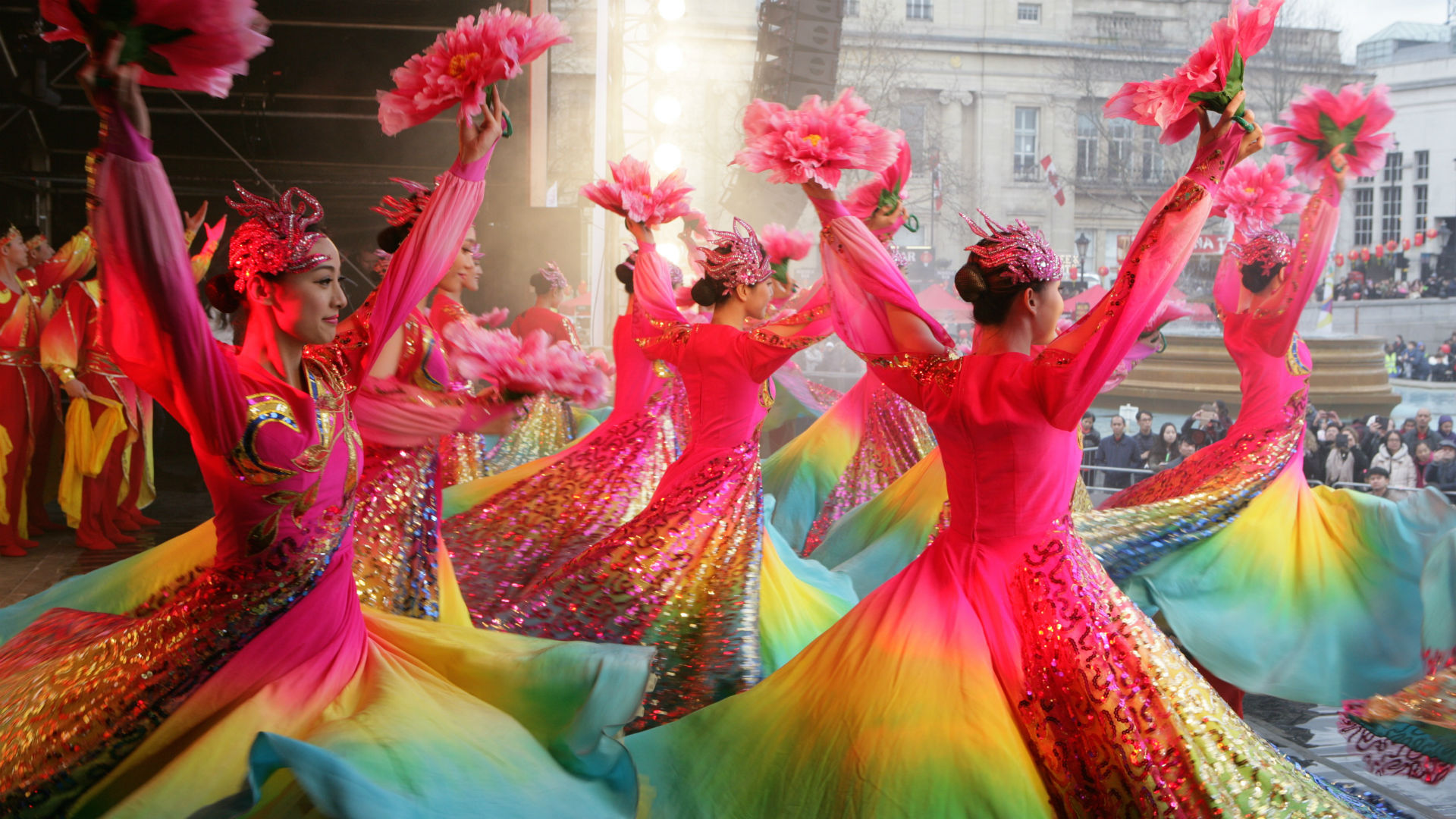 A group of brightly dressed dancers perform on a stage in front of crowds in Trafalgar Square during Chinese New Year in London