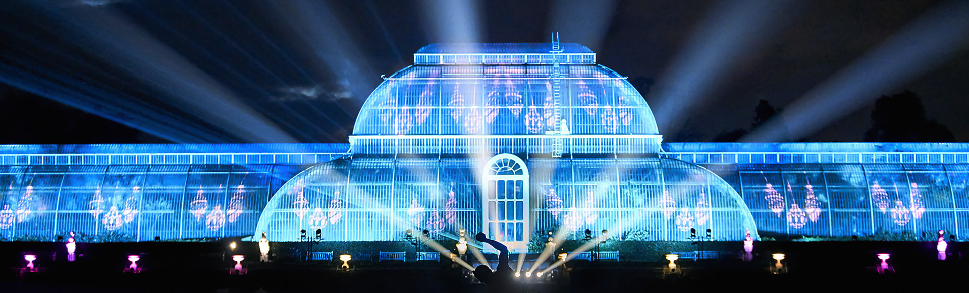 The Palm House at Kew Gardens lit up in blue and purple at night