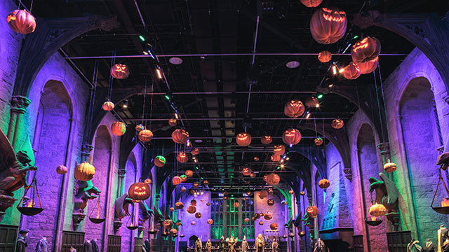 Floating orange pumpkins hanging from the ceiling of the Great Hall, lit up in green and purple light
