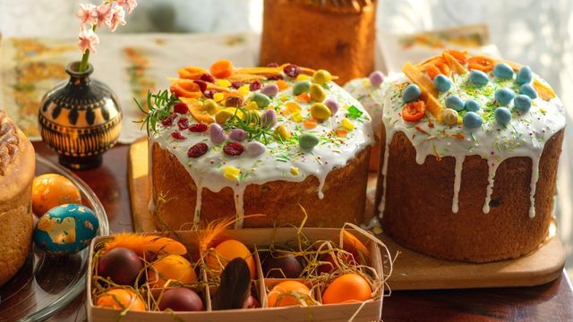A tray of orange eggs in straw and two large easter cakes with colourful eggs and white dripping icing. 
