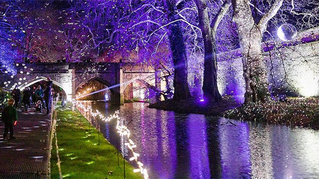 Purple and white illuminations light up the water and bridge over the ancient moat at Eltham Palace.