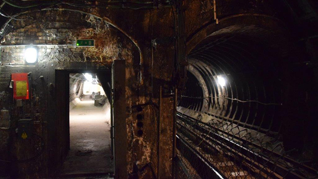 A dimly lit, disused Tube tunnel, track and platform that's lit only by two lights.