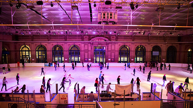 People ice skating in the evening under purple and yellow lights at the Alexandra Palace ice rink