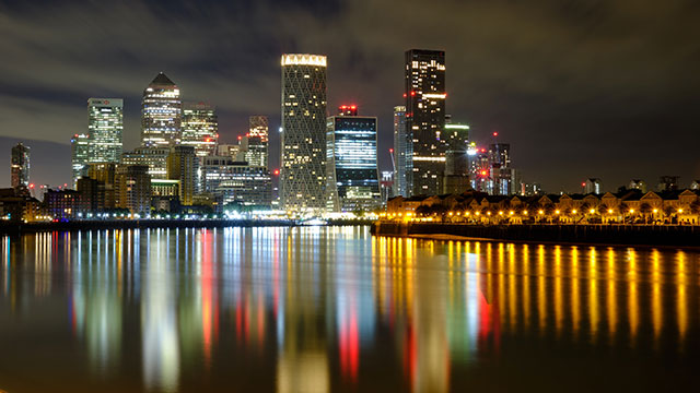 Canary Wharf at night with the office buildings lit up in many colours and reflecting on the water.