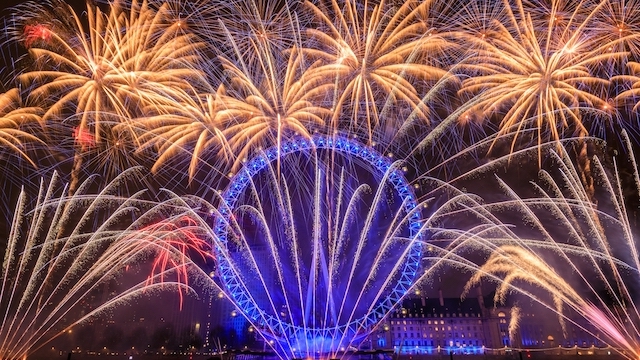 Fireworks for New Year's Eve in London light up the sky behind the blue glowing London Eye.